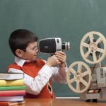 Little Boy Filming With Video Camera In Front Of Blackboard